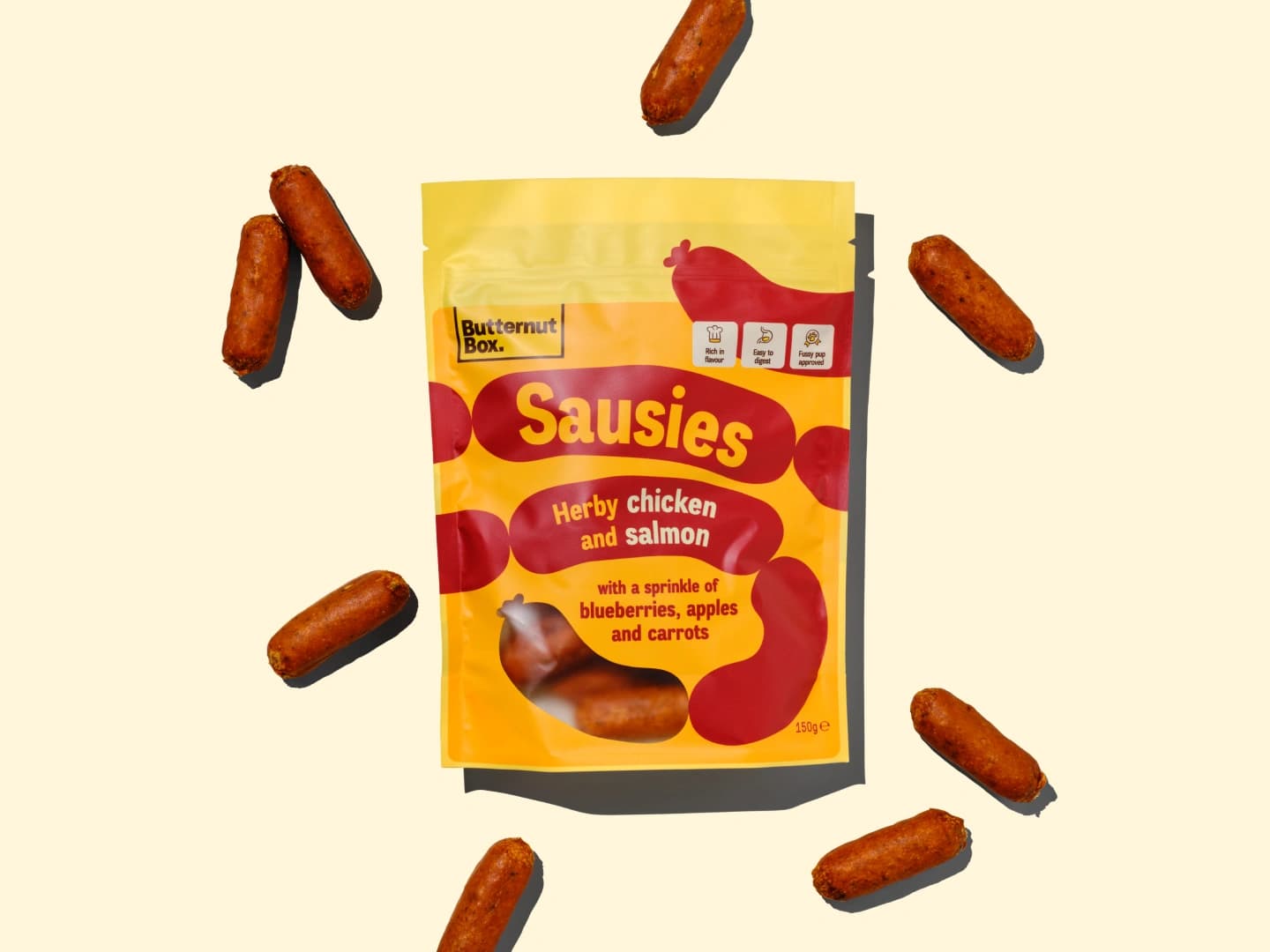 Butternut Box Sausies pack with Herby Chicken and Salmon flavor, surrounded by small sausage treats on a light background.