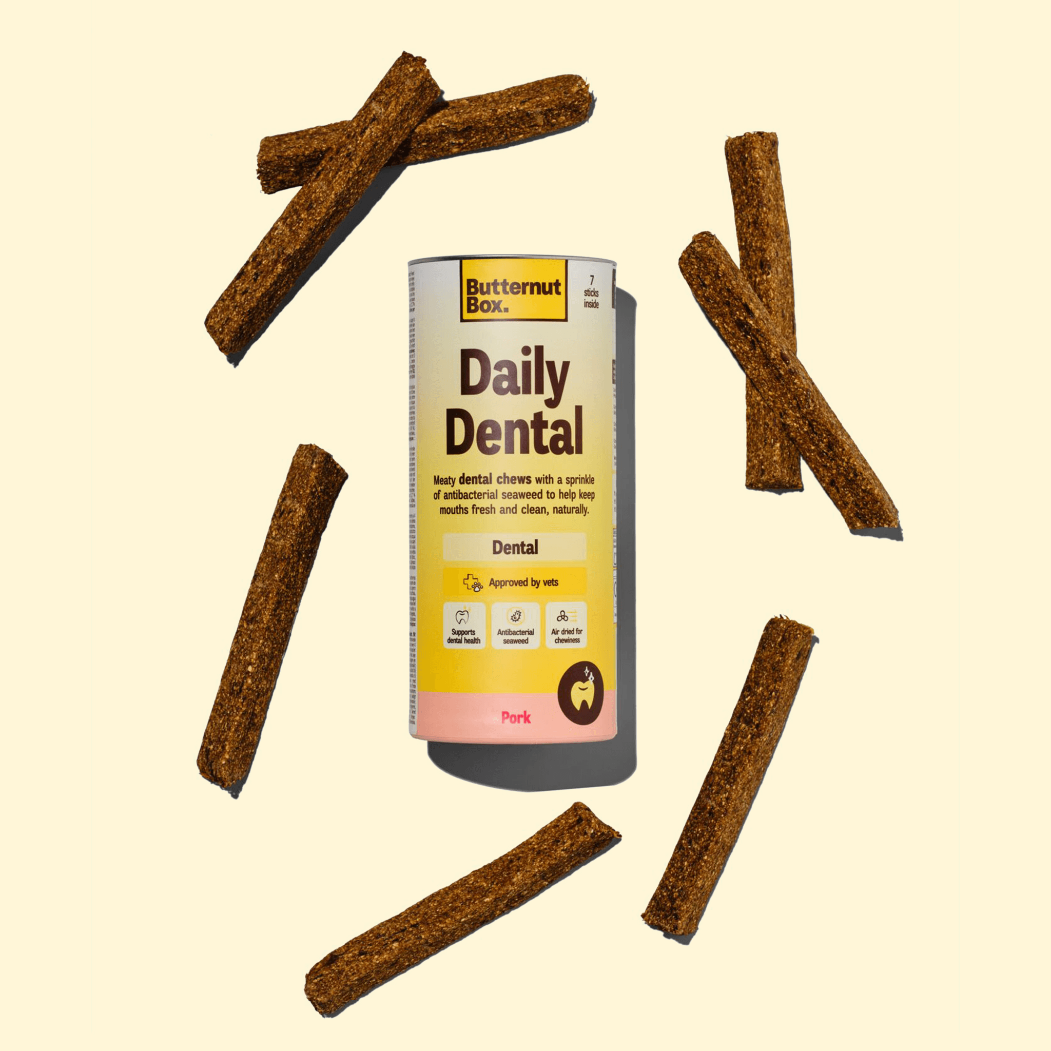 Butternut Box Daily Dental chews package surrounded by six dental sticks on a light background.